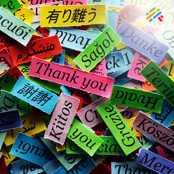 The word 'thank you' handwritten on colorful torn paper strips in more than a dozen different languages and scripts.